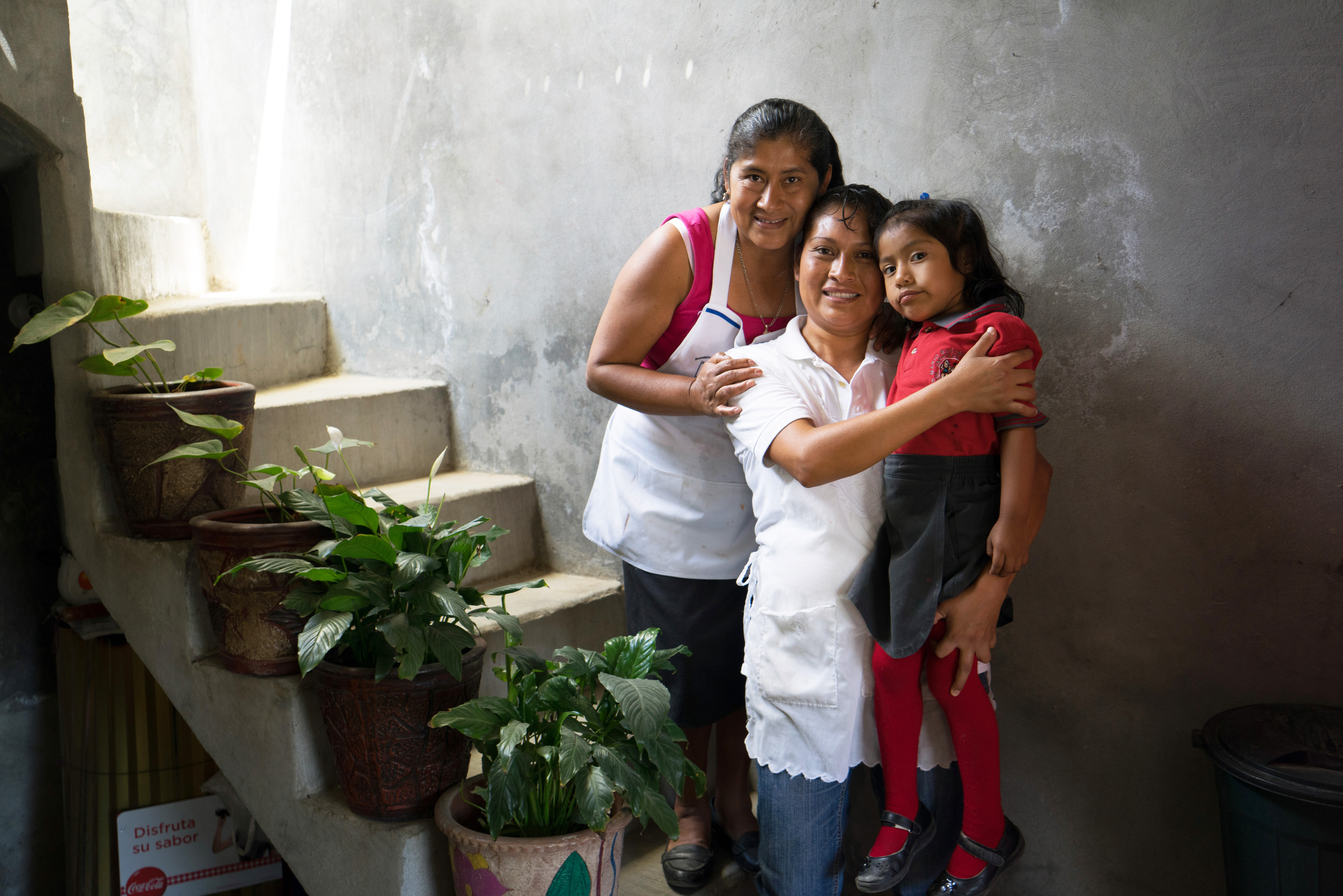 Two women and a young girl stand on a staircase while embracing each other.