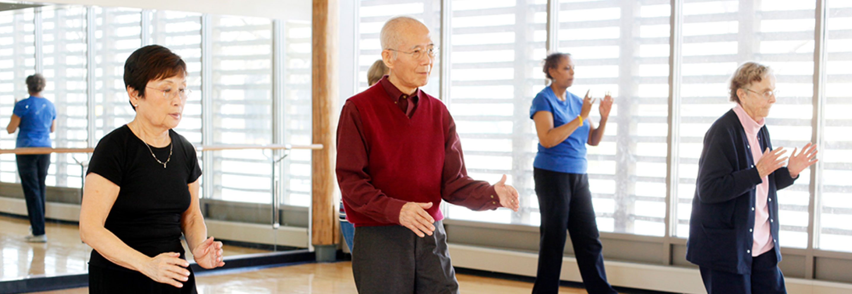 Elderly people practice thai chi in a room with mirrored walls