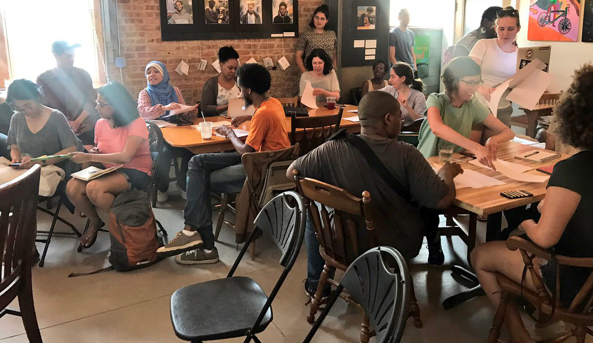 large group of people collaborating together at several tables in a bright space
