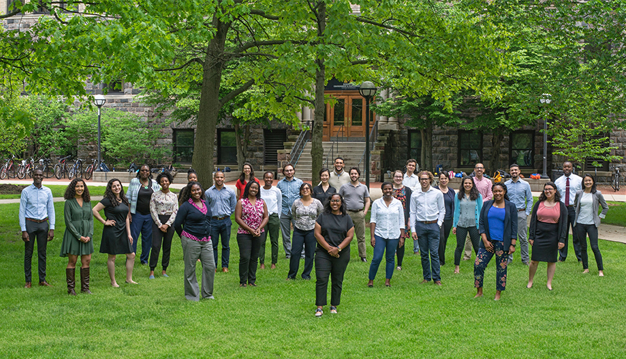 A group of diverse people stand on grass under trees and pose for a picture.