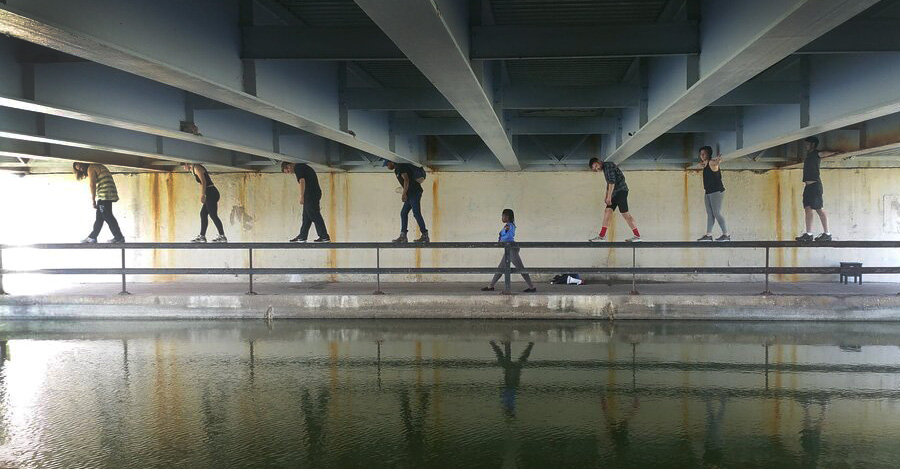 A group of people under a bridge walking on a railing next to water.