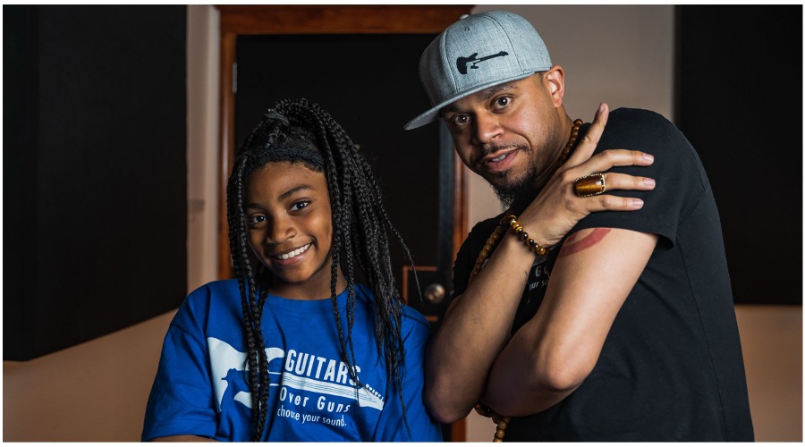A smiling Black girl and a Black man with a gray hat that has a guitar symbol pose for a picture.