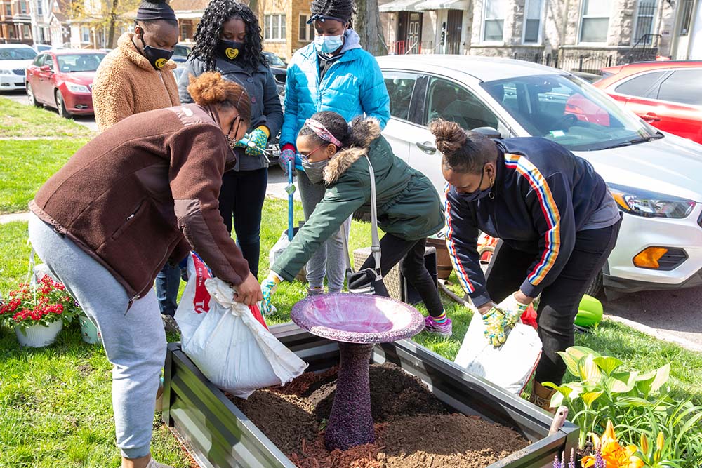 A group of women and girls pouring soil into a container to plant flowers.