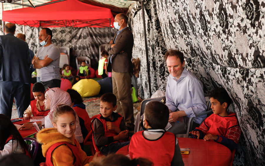 A group of children and adults sitting at desks with people standing in the back.