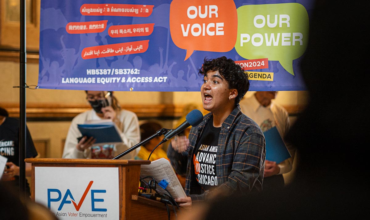 Person speaking at a podium with a banner that reads