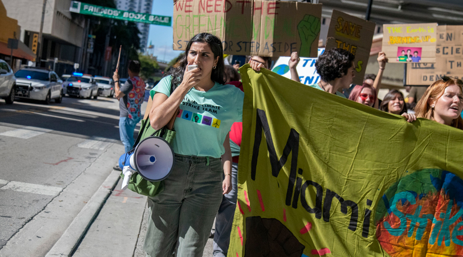 A person talking into a megaphone while holding a banner with other young people at a climate protest.