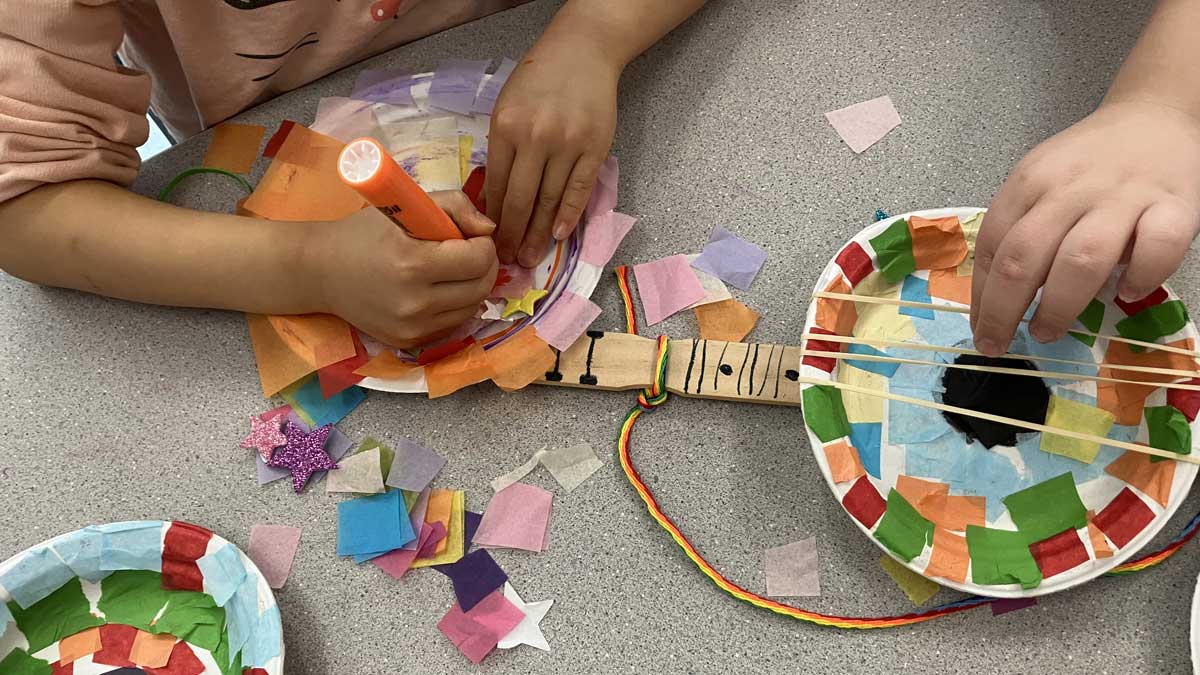 Children making a colorful stringed instrument from disposable plates and tissue paper.