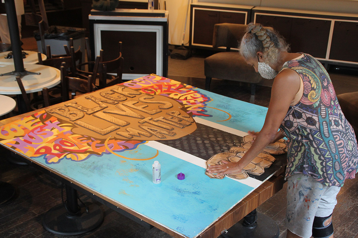 Black woman artist constructing a Black Lives Matter mural in storefront