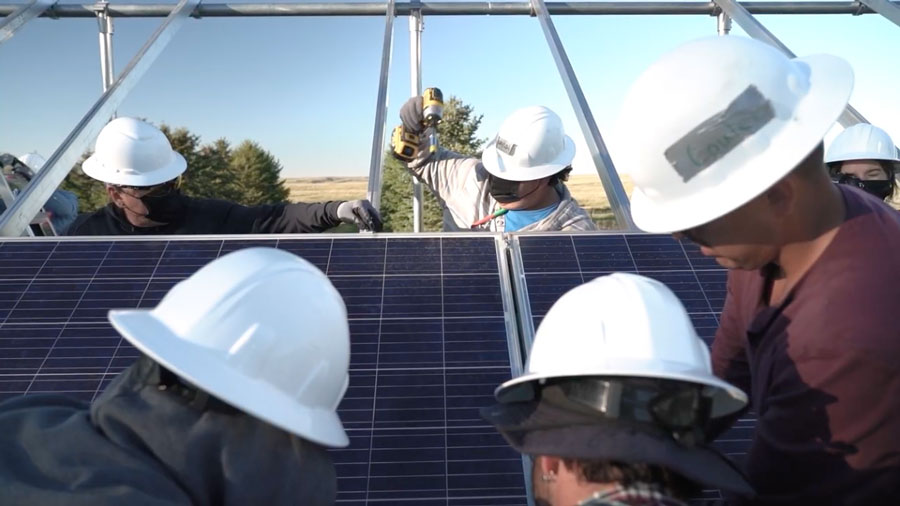 A group of people in safety helmets installing solar panels outdoors.