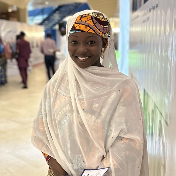 Person wearing a white scarf and a colorful hat, smiling indoors at an event.