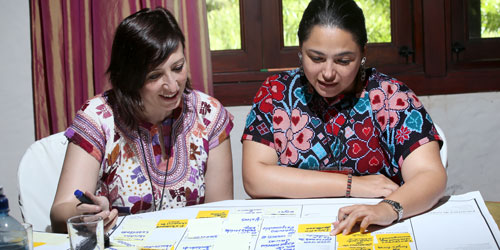 Two women discussing notes on a table with sticky notes and a notebook in the background.