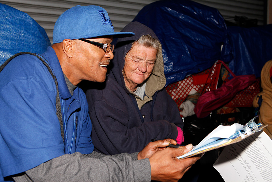 Black man with tablet speaking to homeless woman