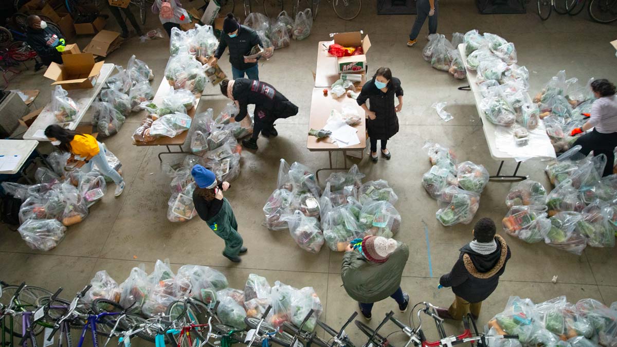 People organizing groceries in plastic bags in a large indoor space with bicycles lined up at the bottom.