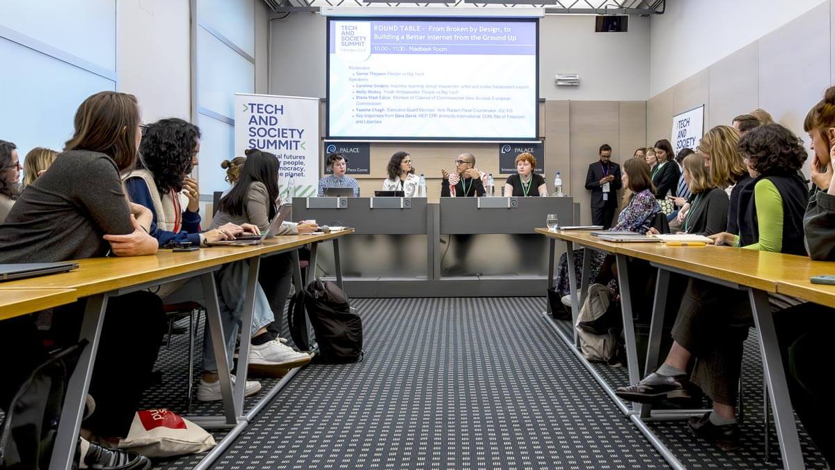 A conference room with panelists speaking to an attentive audience at the Tech and Society Summit.