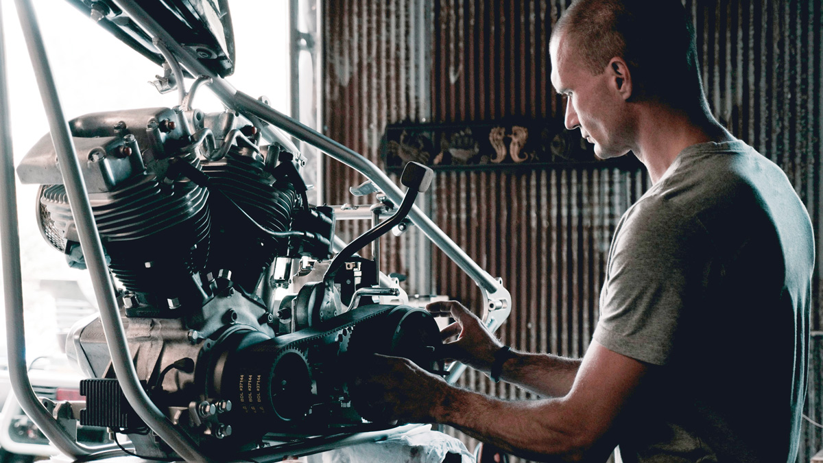 A man examines a large engine in a workshop with corrugated metal walls.