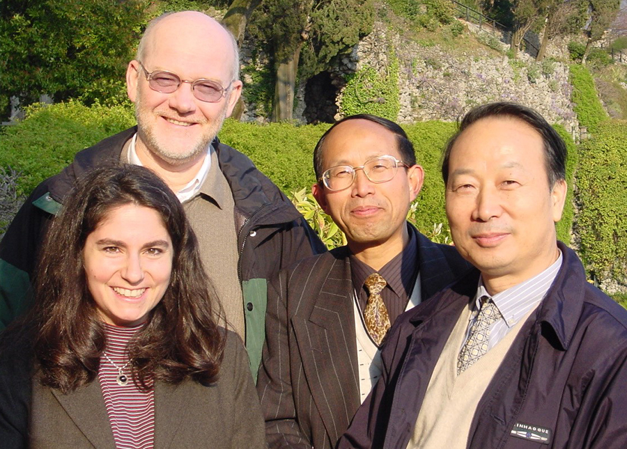 A woman with brown hair smiles poses for a picture with three men, all smiling at the camera.