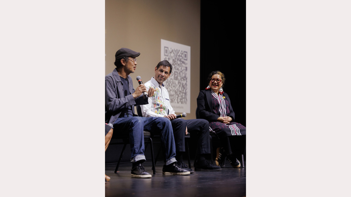 Two men and a woman sit in conversation during a film debut. All three are smiling and deeply engaged the discussion.