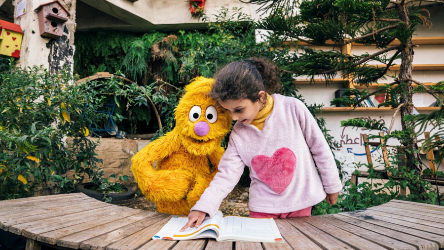 A child looking at book with a muppet puppet.