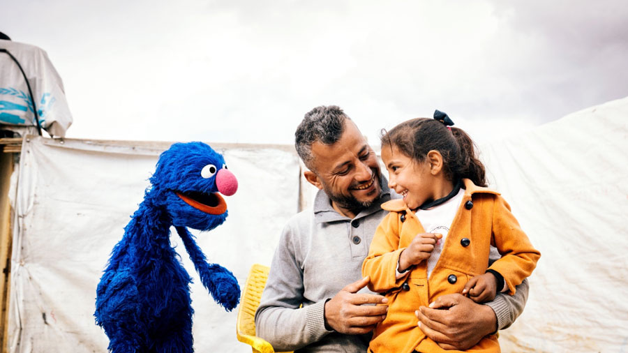 A man holding a child talking to a blue puppet