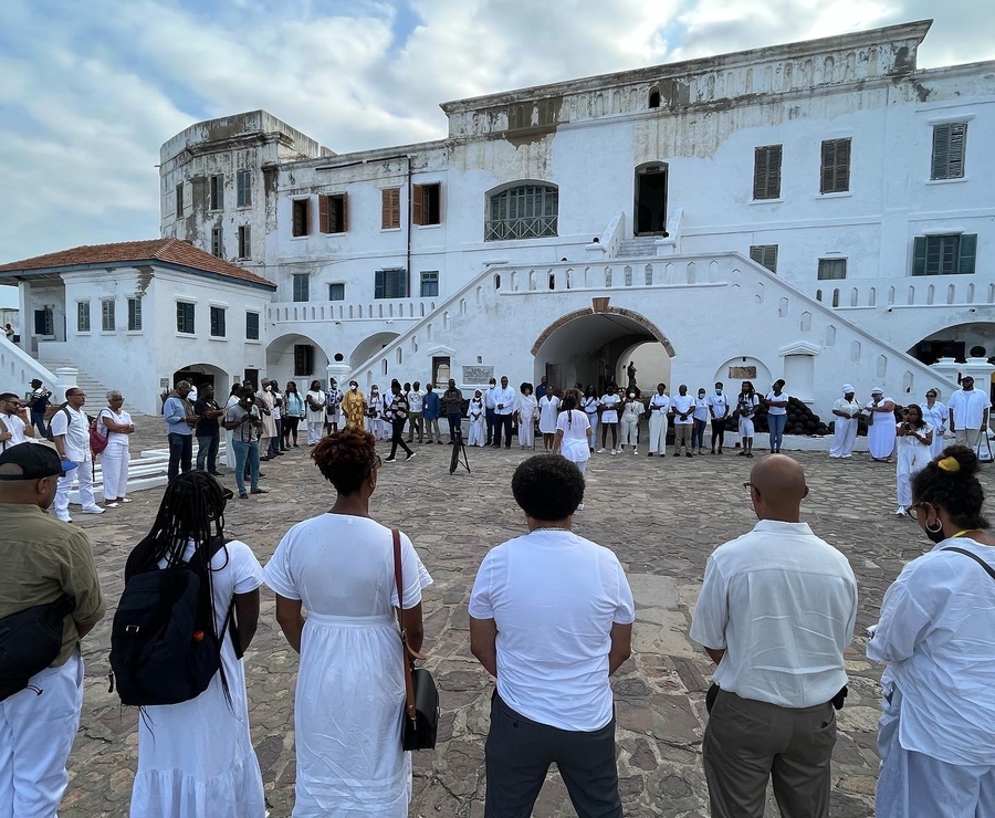 Large group of people dressed in white in foreground, large white building in background