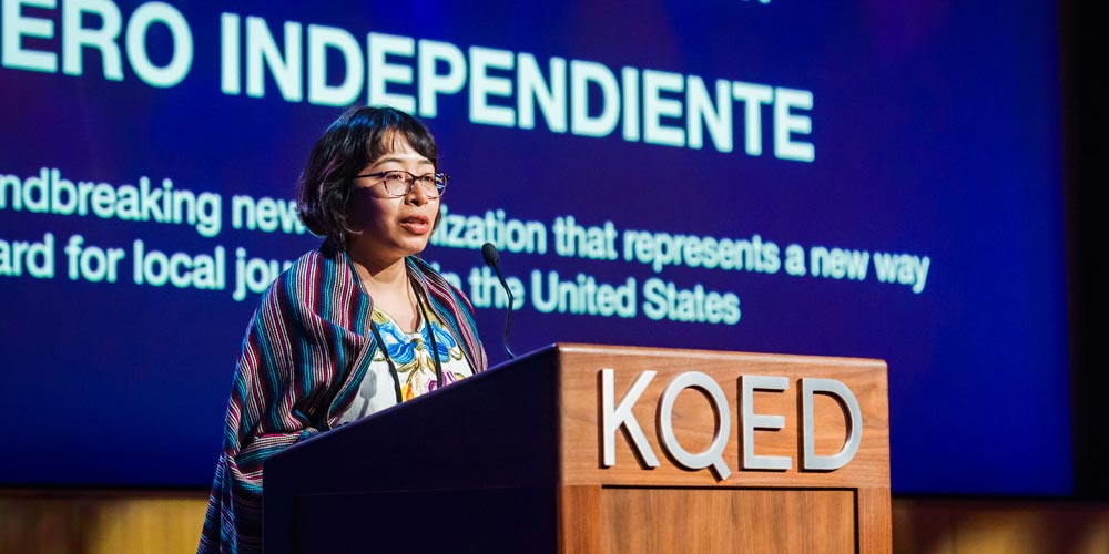 A journalist stands at a wooden podium to accept a local news award. 