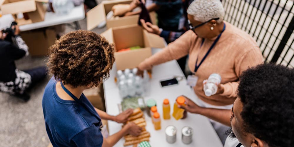 A picture shot from above of three volunteers at a food bank. The workers set out bottles of water and juice, and other snacks. 