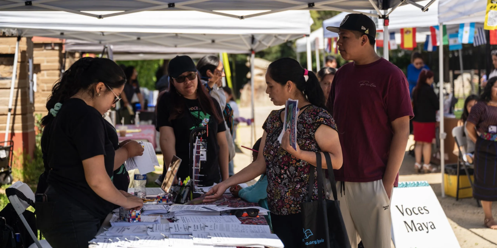 A gathering of people stands around a booth, gathering helpful documents at a community resource fair. 