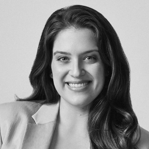 A shoulders-up, black-and-white portrait of Isabella Ulloa, President, Foundation for Public Service. She wears a sharp blazer and smiles.