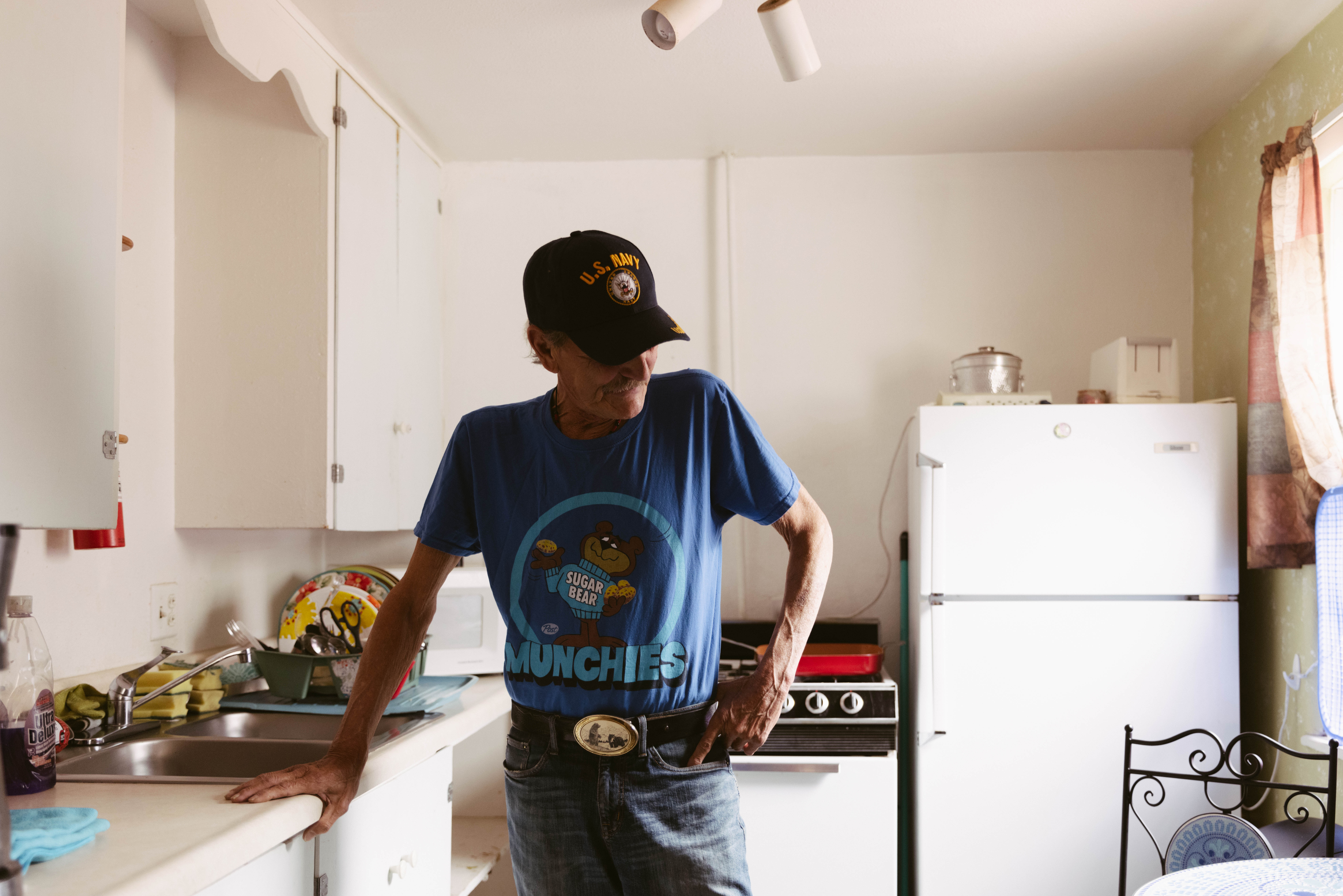 A man standing in a kitchen looking down with a US Navy cap on.