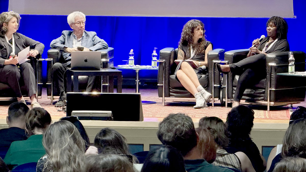 A panel discussion with four speakers seated on stage with a blue background.