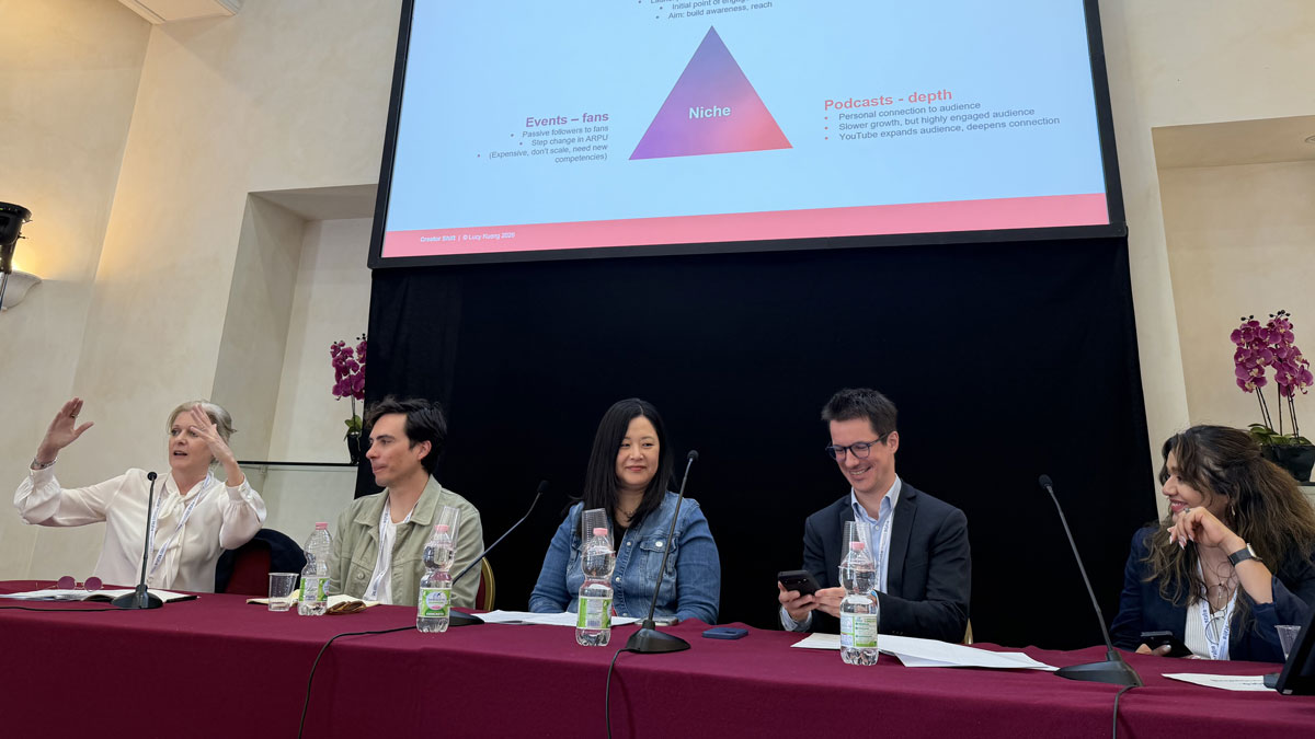Five panelists sit at a table during a discussion, with a slide projected behind them.