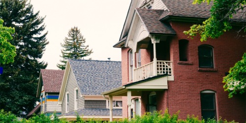 Three colorful houses with porches and gabled roofs, surrounded by green trees and bushes.