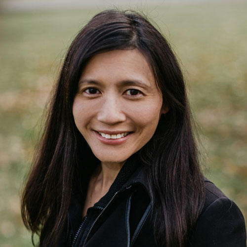 A shoulders-up photo of Karen F. Lee, Executive Director & Founder, FedsForward. She has long black hair smileing warmly while standing in a lush green park.