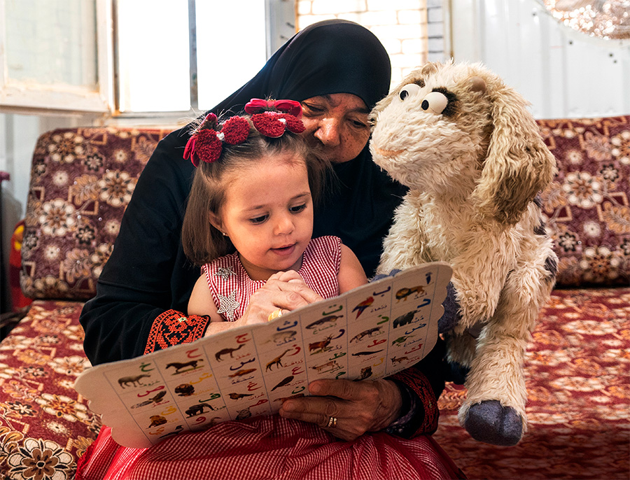 Mother in black headscarf with young girl learning to read and furry goat muppet