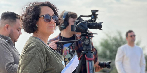 Group of people outdoors, one operating a camera on a tripod.