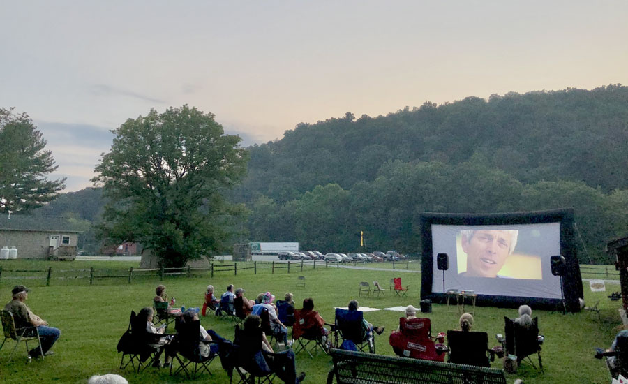 A group of people sitting in a field in front of a large screen.