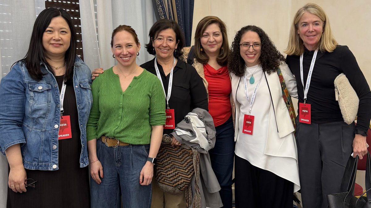 Six women with speaker badges stand together, smiling, in front of curtains.
