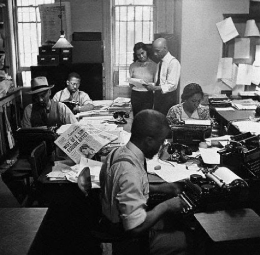 Black and white photo of a busy newsroom with people working at typewriters