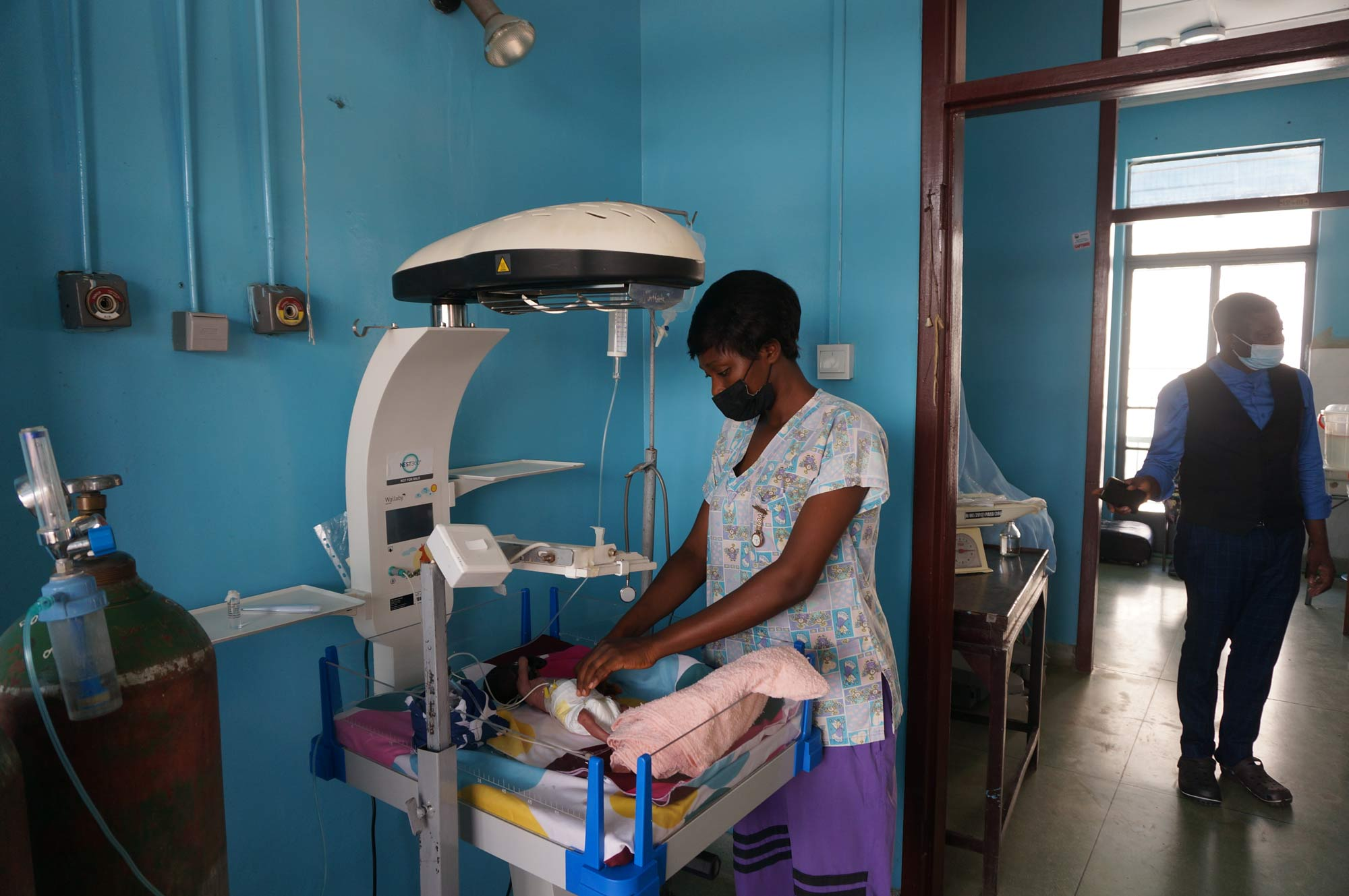 A woman nurse uses a phototherapy machine to treat a baby in a hospital room.