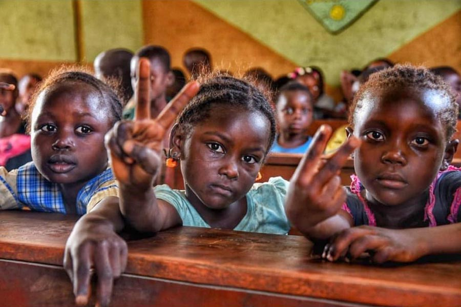 close-up shot of three children's faces, two of the children are doing a peace sign hand gesture.