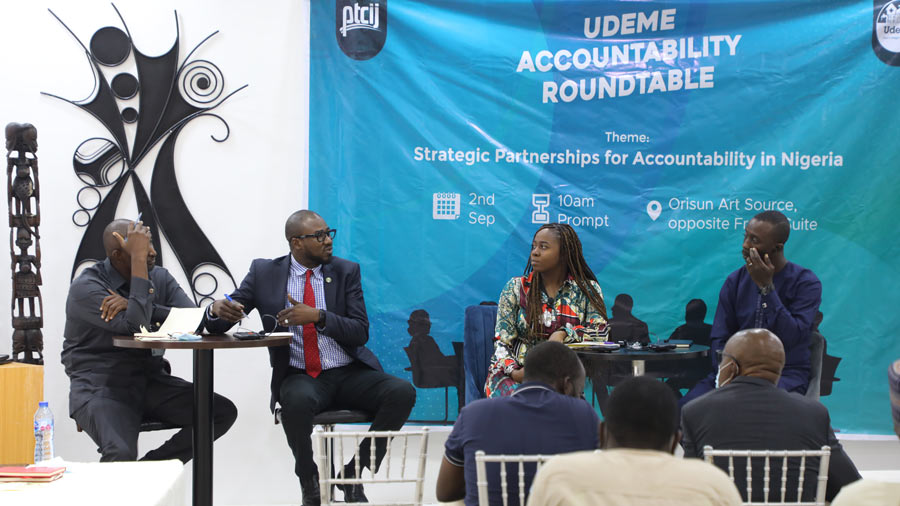 four people on a stage, in front of a banner, having a discussion