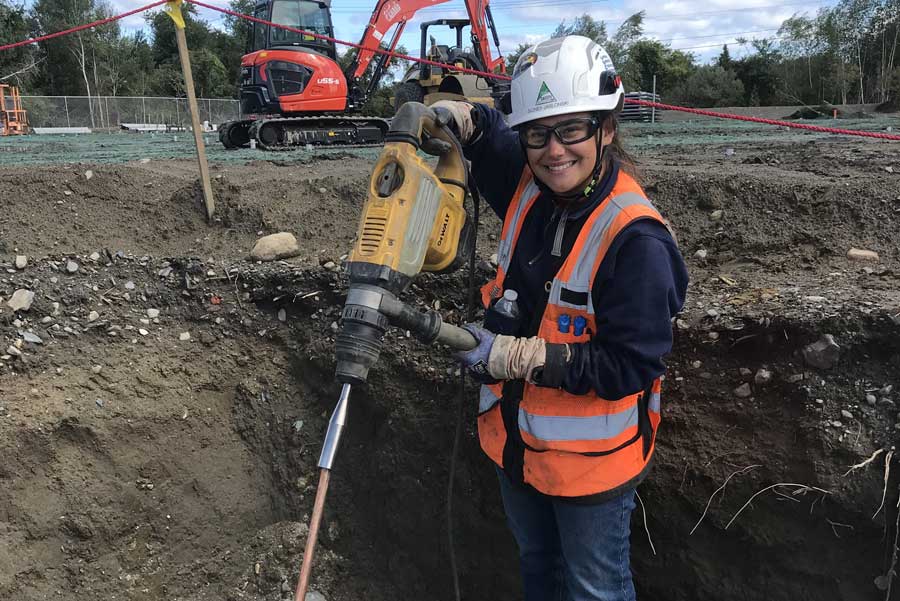 A woman holding a jackhammer smiles for the camera.