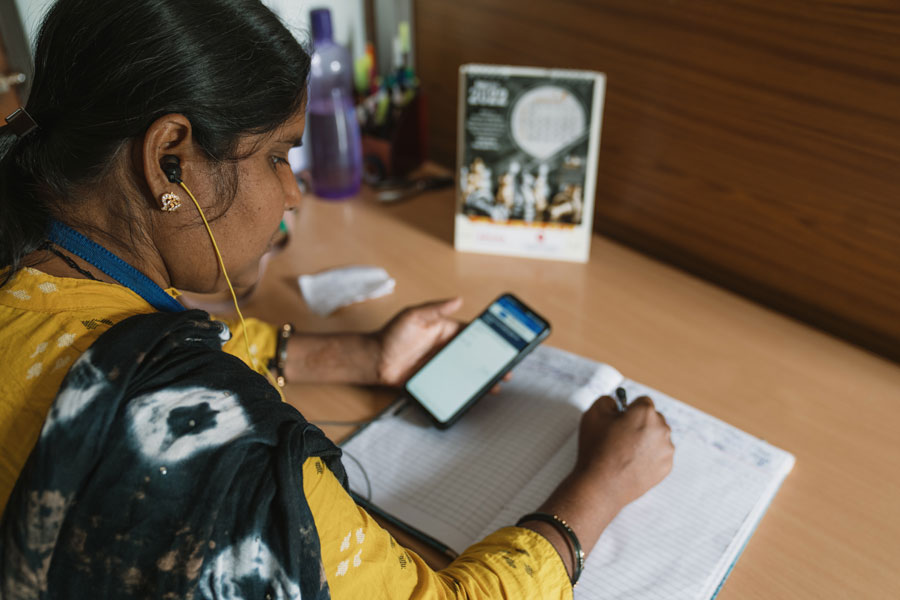 A person holds a phone while making notes in a notebook.