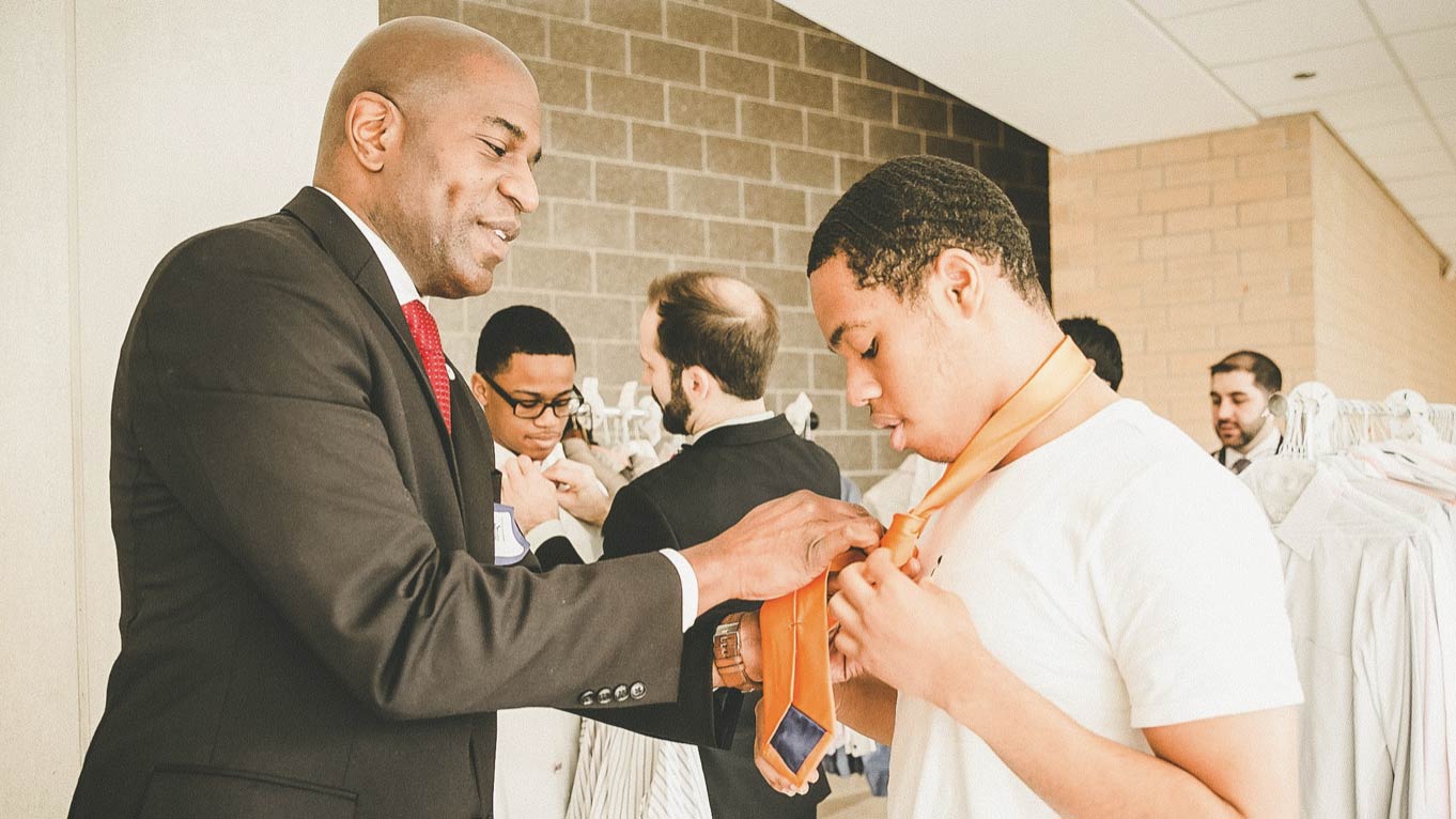 A man helping a young man tie his neck tie