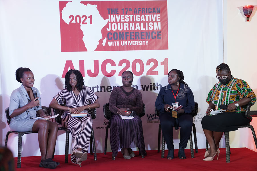 five people seated on a stage, in front of a banner, having a discussion