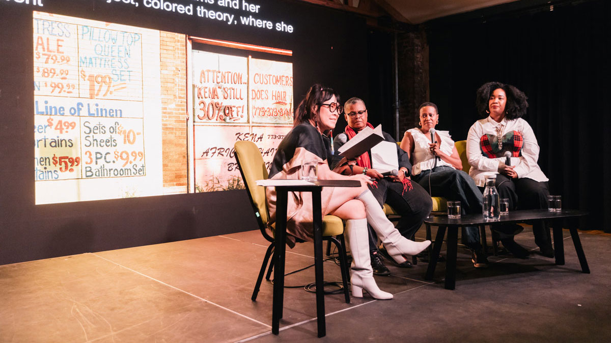 A quartet of women sits in a row of chairs for a panel discussion. Each woman holds a microphone.
