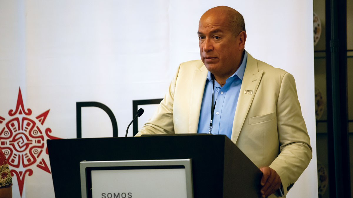A man in a light suit speaks at a podium with a microphone.