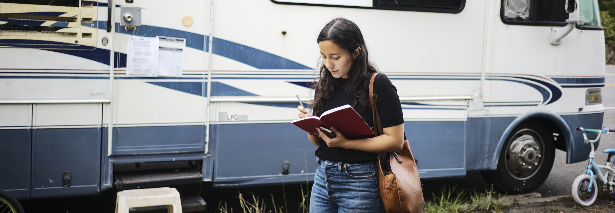 Woman writing in a notebook in front of a parked RV.