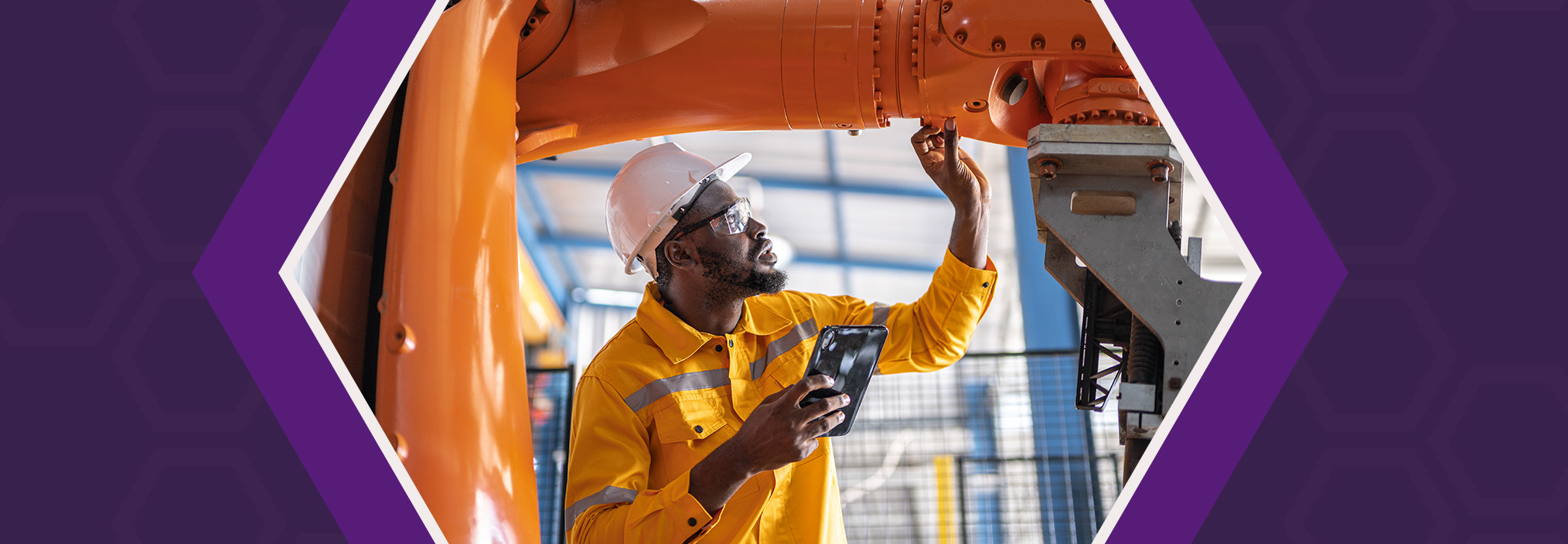 A man in a safety outfit inspects an orange industrial machine while holding a tablet.
