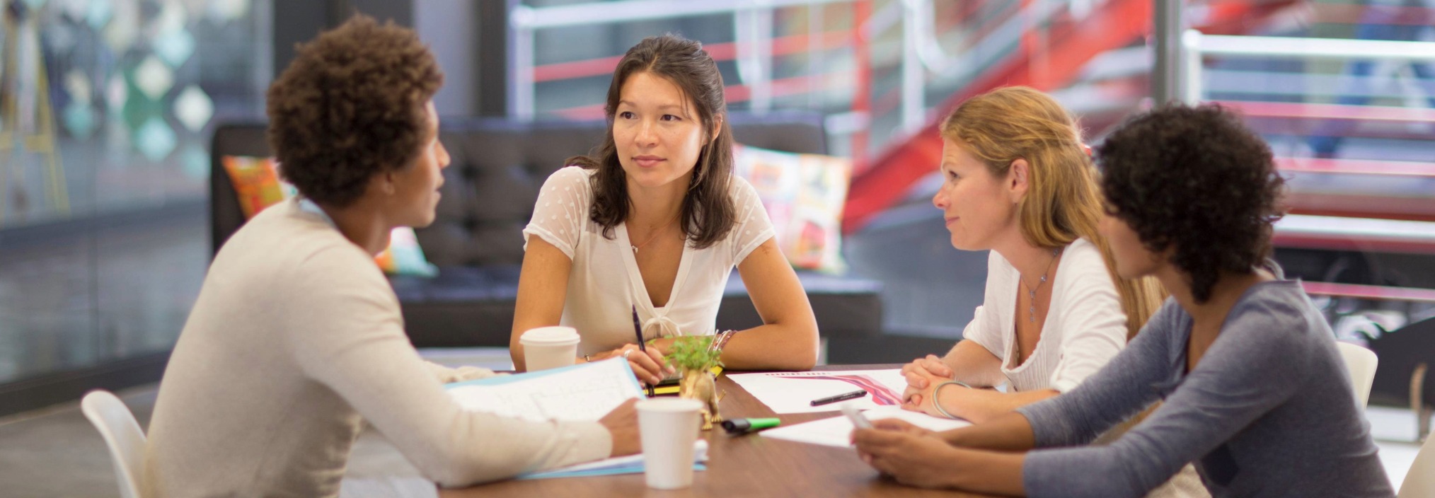 Four people sit around a table in discussion, with papers and coffee cups in a modern office setting.